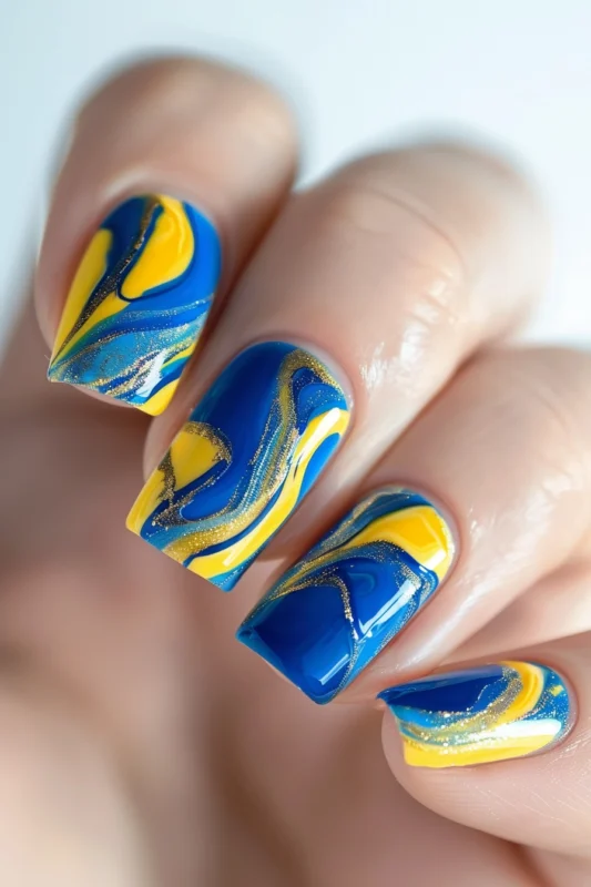 Square-shaped nails with blue, yellow swirls, and golden glitter accents.