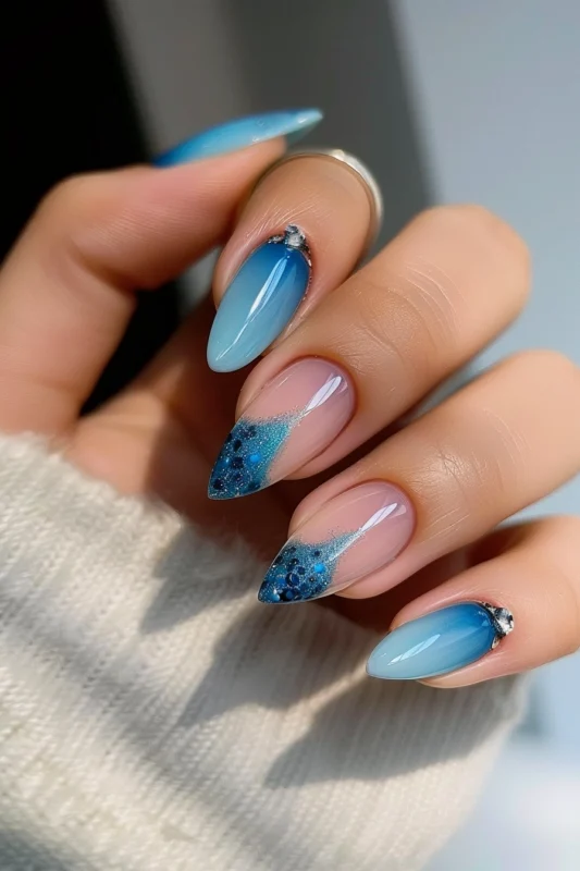 Almond-shaped nails with blue gradient French tips and blue ombre nails embellished with glitter and rhinestones.