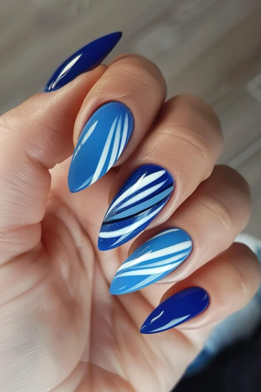 Stiletto nails in various blue nail polishes covered with white striped patterns.