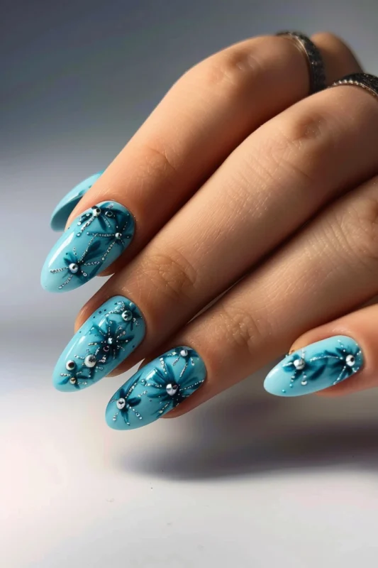 Ocean blue rounded nails with dark florals, silver gems, and silver accents.