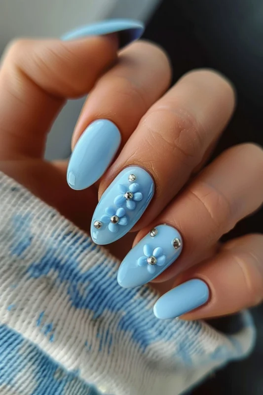 Pastel blue nails with silver bead accents and flower decals.