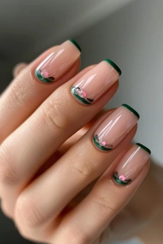 Nude nails with green tips and edges and small floral designs.