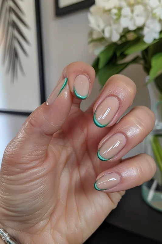 A hand with nails outlined in light and jade green on a nude base.