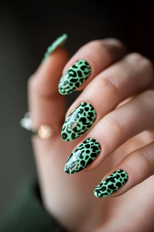 A hand with almond-shaped nails in a glossy emerald green leopard print design.