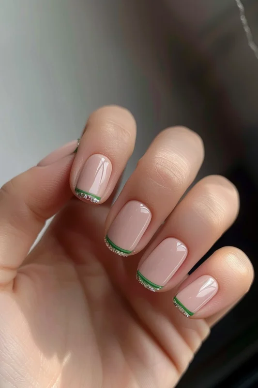 A hand with short, square-shaped nails featuring vibrand and forest green French tips lined with glitter.