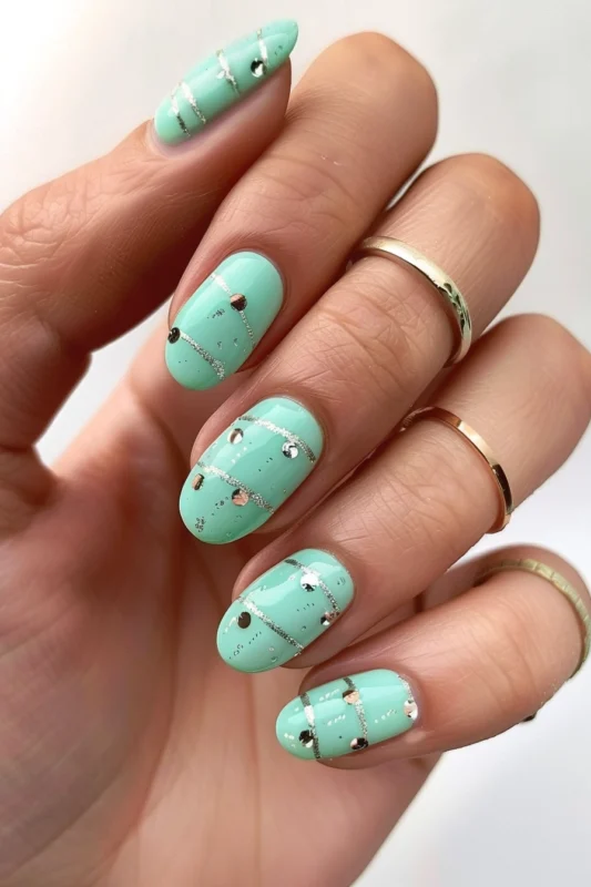 Short rounded mint green nails with glitter and studs.