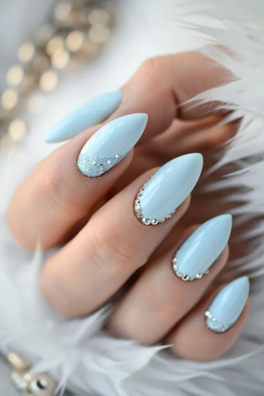 Baby blue nails with glitter tips and crystal bead accents.
