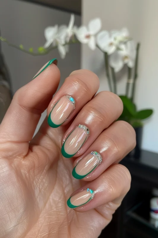 Nude nails with matte jade green tips and silver glitter detailing at the base.