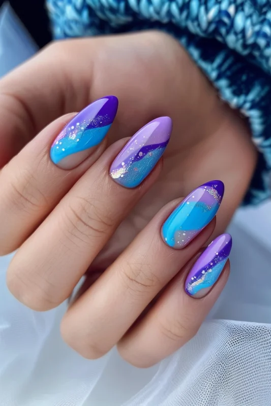 Almond-shaped nails with a blue and purple gradient and glitter.