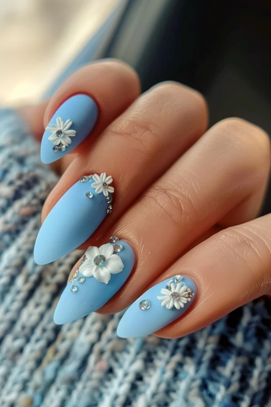 Matte light blue nails with white flower details and rhinestones.