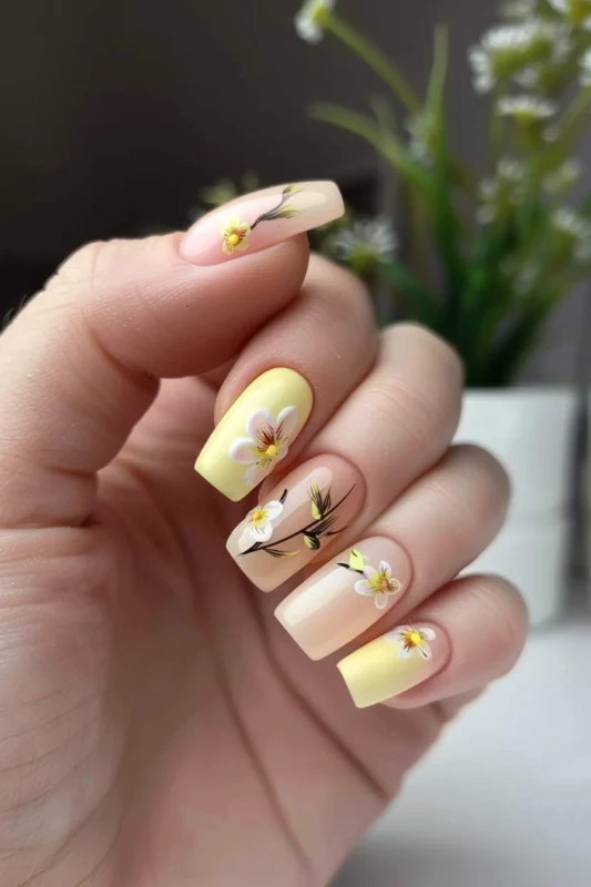 Nails with a gradient of yellow and pink, with white floral accents.