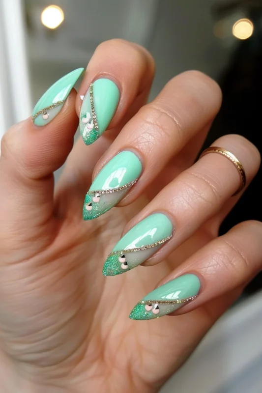 Mint green nails with green glitter French tips and gold chain and gem details.