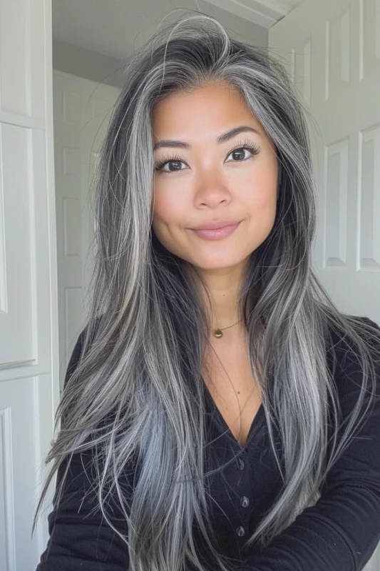 A young woman with long salt and pepper hair, featuring darker roots and silver ends.