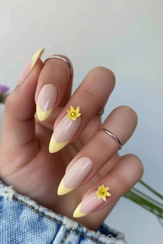 Pastel yellow French tips with small yellow flower accents on accent nails.