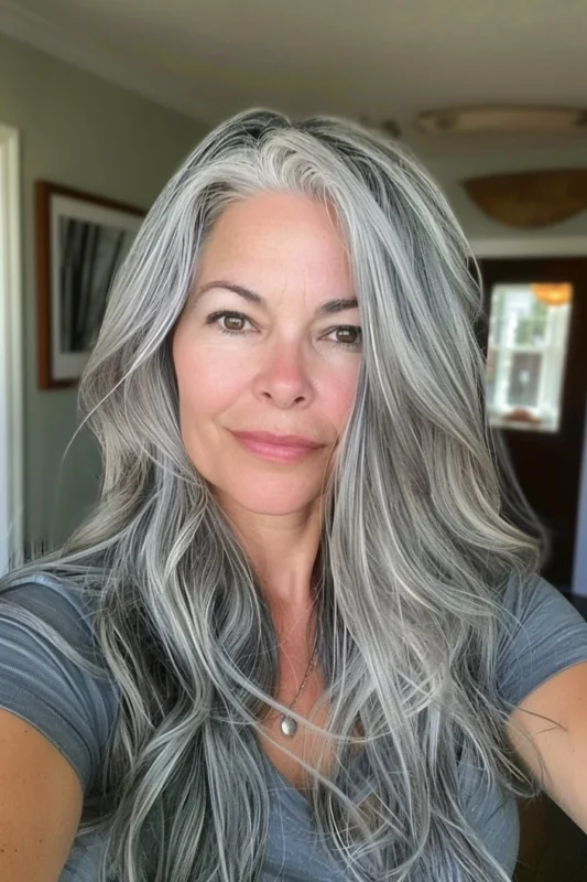 A woman with long wavy salt and pepper hair and darker roots.