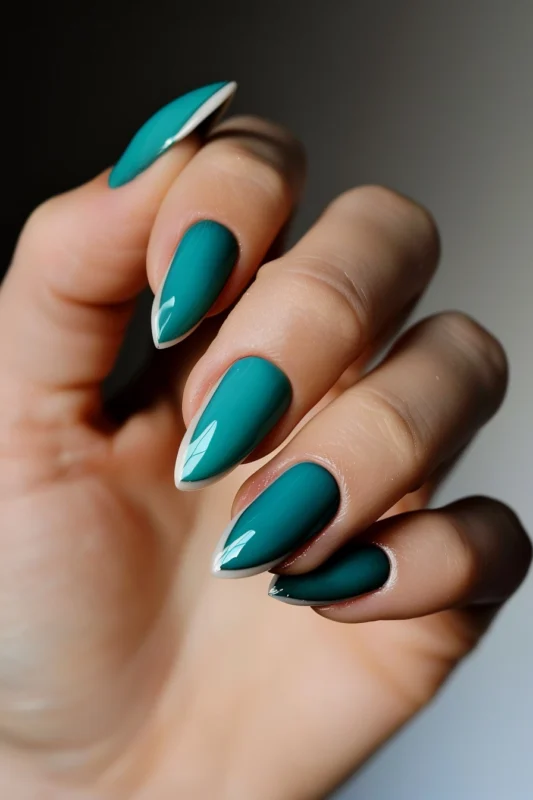 Almond-shaped nails painted in a deep teal polish ending with subtle white French tips.
