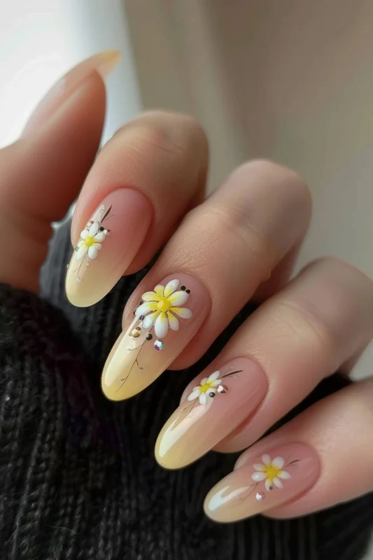Nude and light yellow ombre nails with hand-painted daisies and silver embellishments