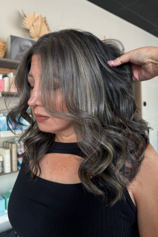 Warm grey highlights on dark brown hair for gray hair blending with elegance.