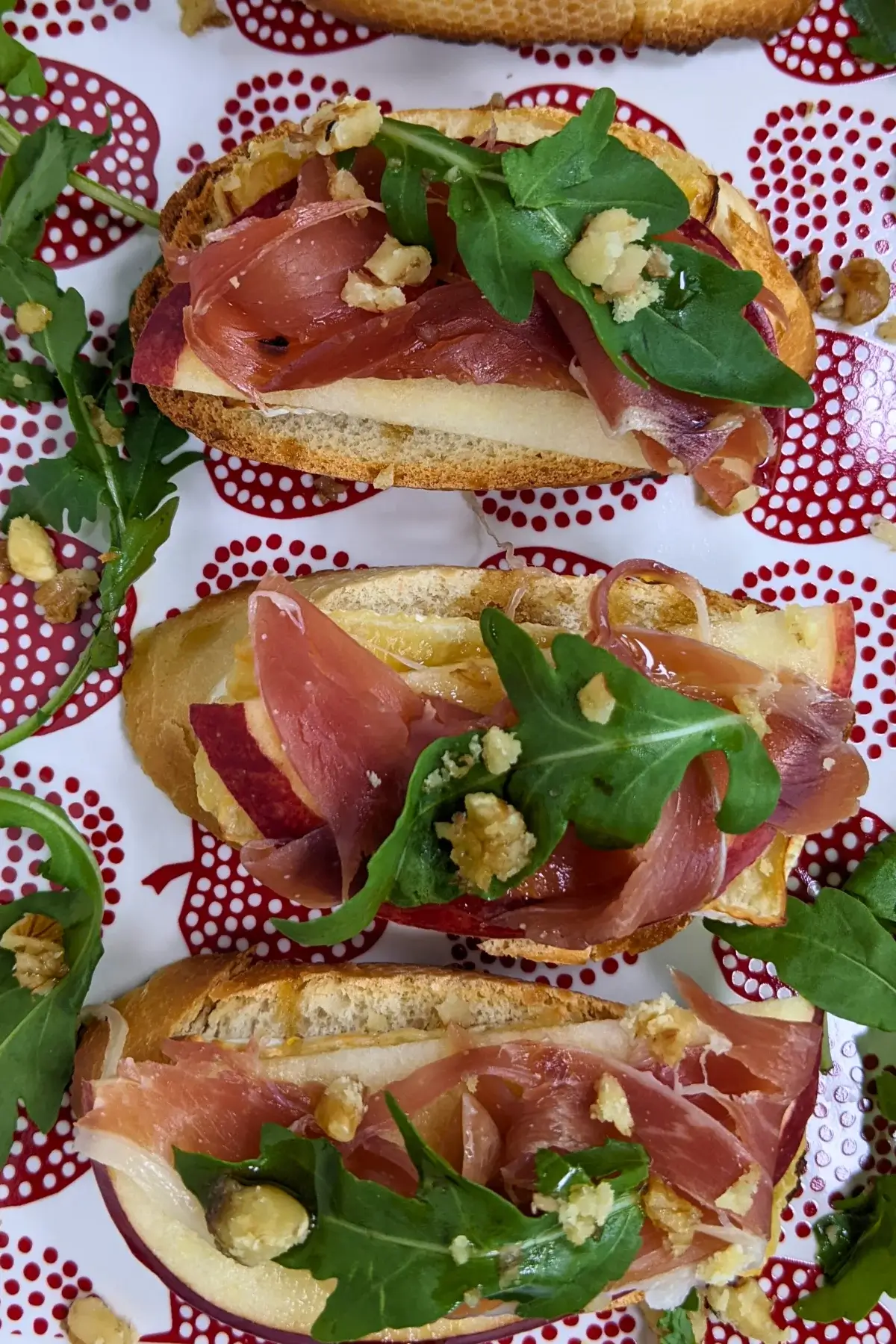 Crostini appetizers with apple, Brie cheese, and serrano ham topped with arugula, crushed walnuts and maple syrup.