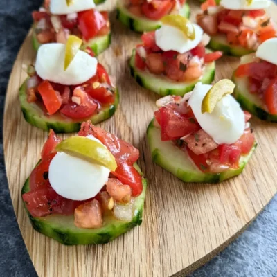 Fresh bruschetta cucumber bites appetizers topped with mozzarella balls and sliced olives, neatly arranged on a serving tray.
