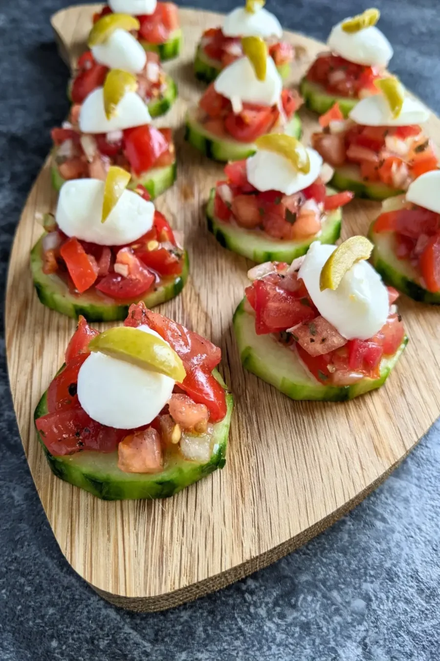 Fresh bruschetta cucumber bites appetizers topped with mozzarella balls and sliced olives, neatly arranged on a serving tray.
