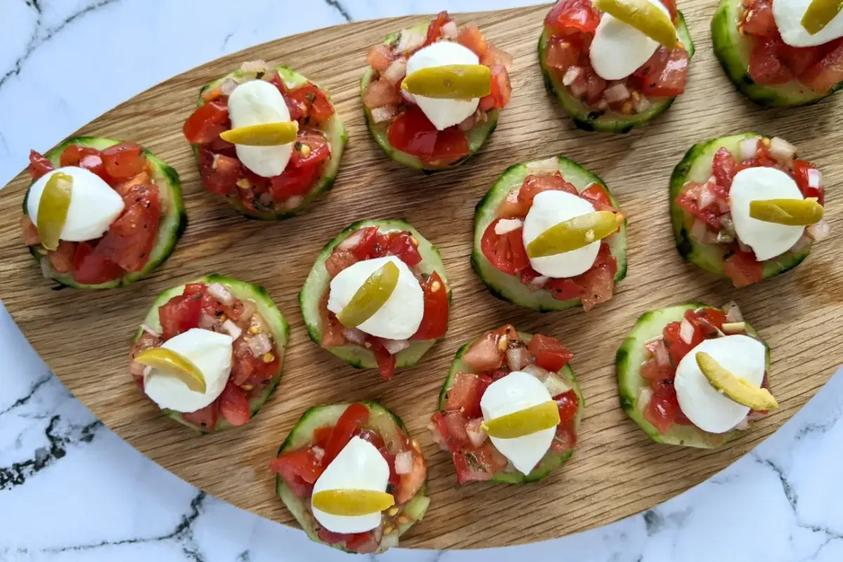 Fresh bruschetta cucumber bites appetizers topped with mozzarella balls and sliced olives, neatly arranged on a serving tray.