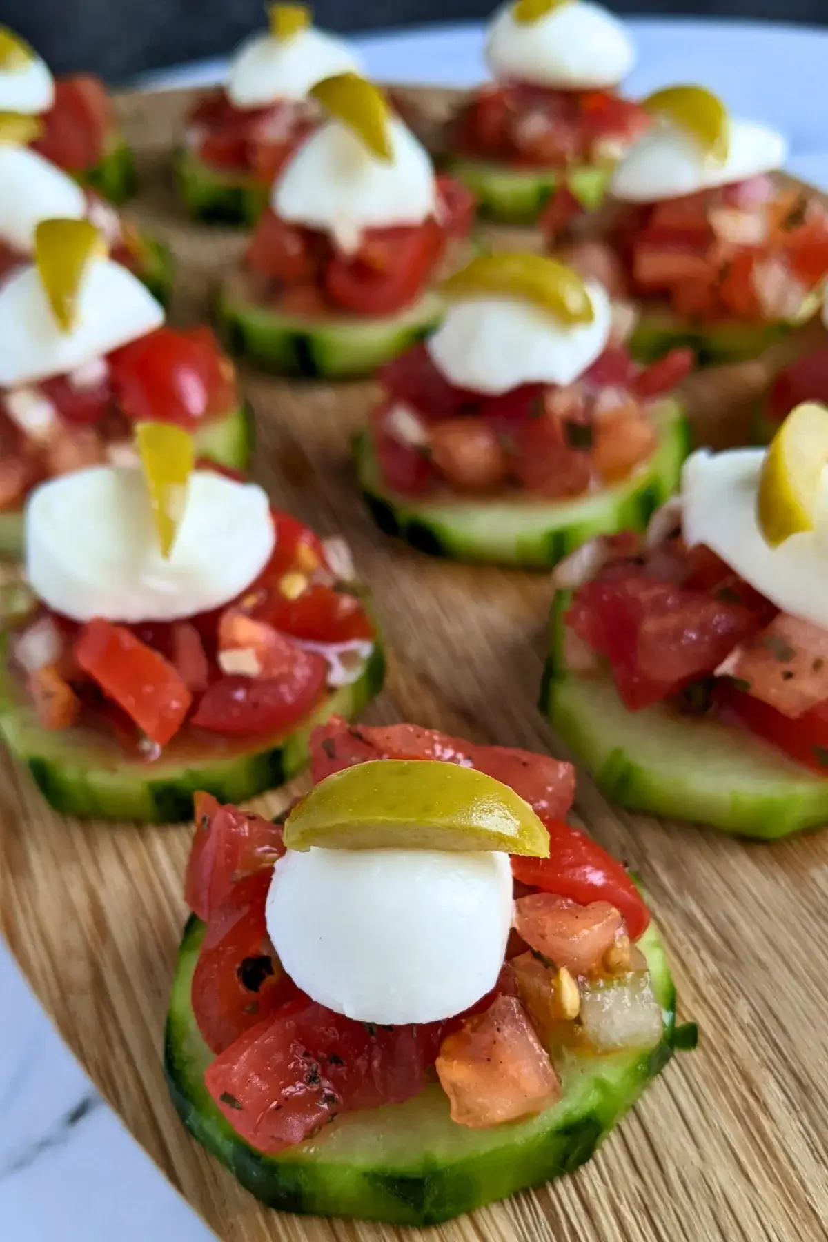 Fresh bruschetta cucumber bites appetizers topped with mozzarella balls and sliced olives, neatly arranged on a serving tray.