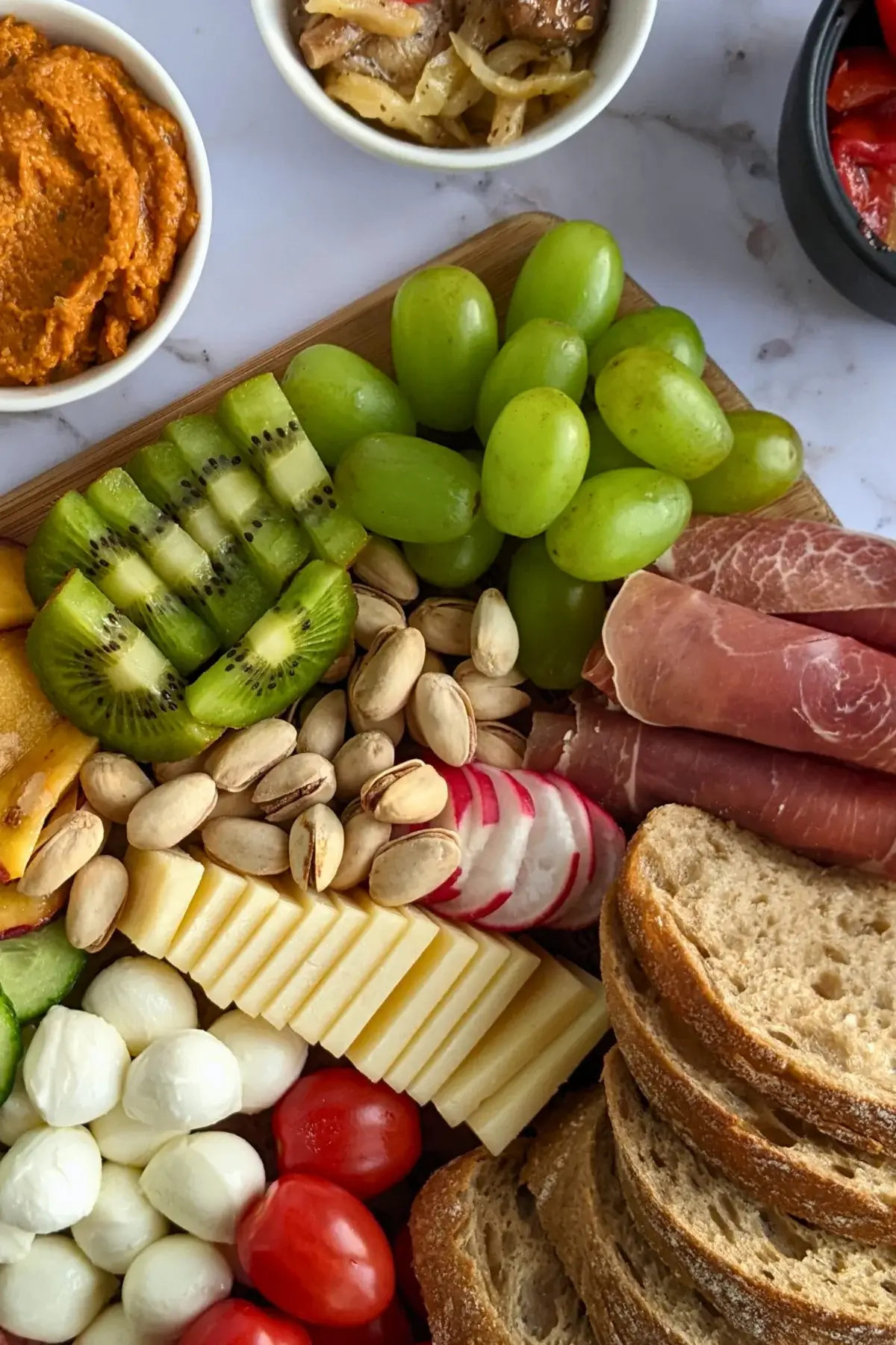 A vibrant colorful antipasto party food platter with cured meats, marinated veggies, cheeses, olives, fruit, and ciabatta arranged on a wooden platter.