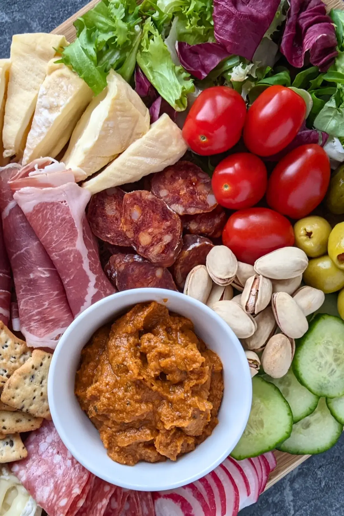 A healthier charcuterie appetizer board featuring fresh vegetables, soft cheeses, sliced meats, and pickled bites on a rustic board.