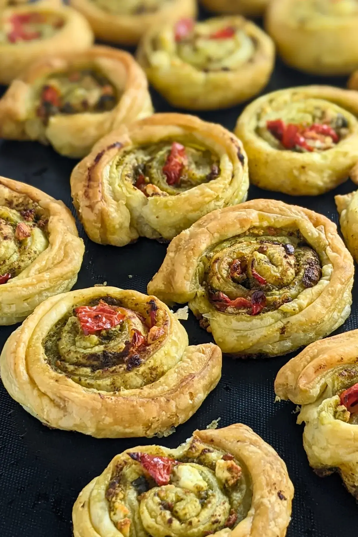Savory pesto pinwheels made with puff pastry and filled with basil pesto, fresh cherry tomatoes, and crumbled feta.