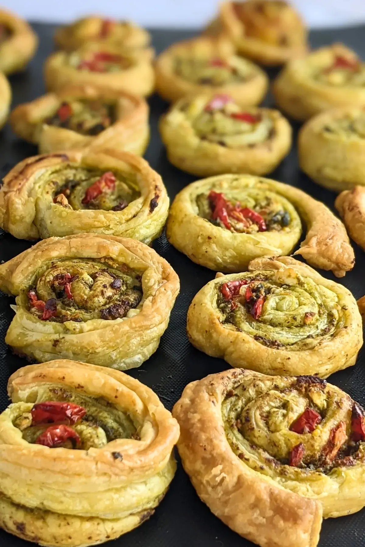 Savory pesto pinwheels made with puff pastry and filled with basil pesto, fresh cherry tomatoes, and crumbled feta.