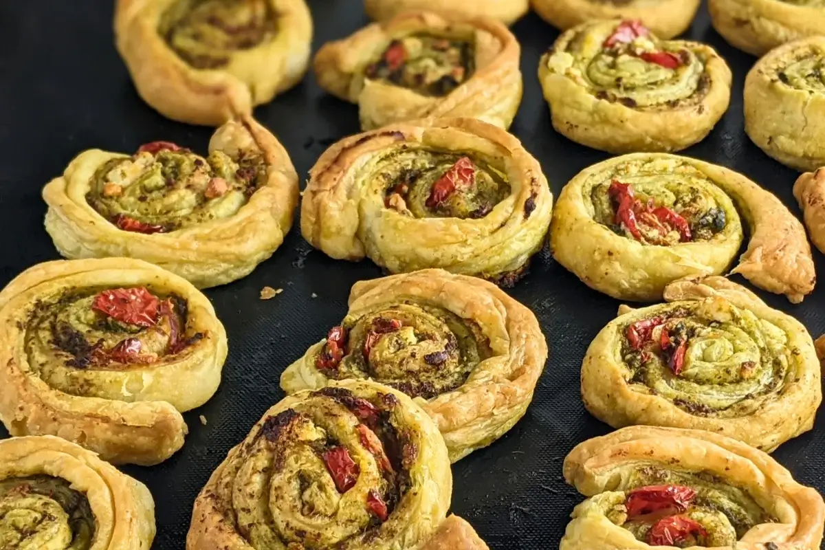 Savory pesto pinwheels made with puff pastry and filled with basil pesto, fresh cherry tomatoes, and crumbled feta.