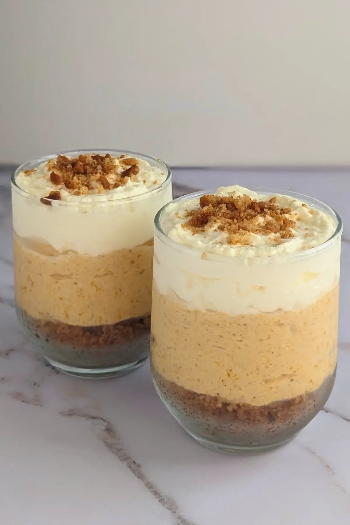 Pumpkin cheesecake mousse cups layered with a cookie and butter base; cream cheese, pumpkin, and whipped cream mousse; and topped with more whipped cream.