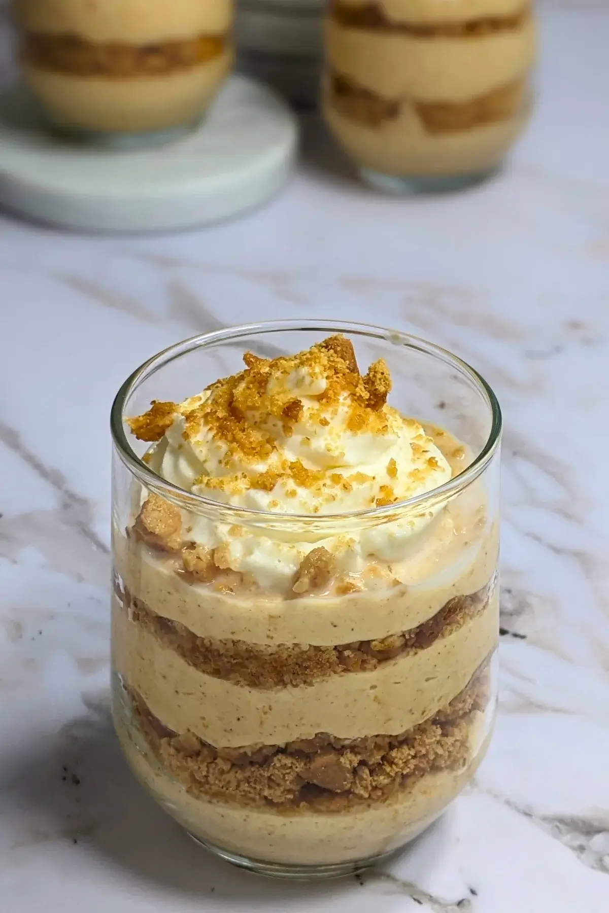 Pumpkin yogurt parfait cups layered with pumpkin yogurt, gingersnap biscuits, and topped with whipped cream.