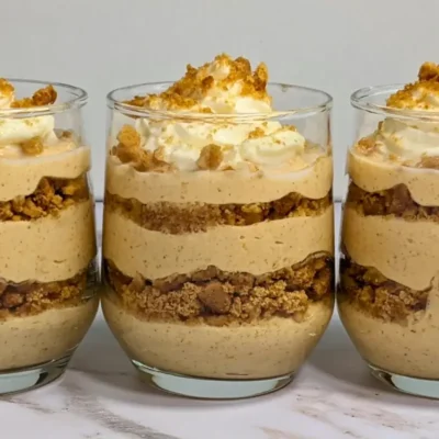 Pumpkin yogurt parfait cups layered with pumpkin yogurt, gingersnap biscuits, and topped with whipped cream.