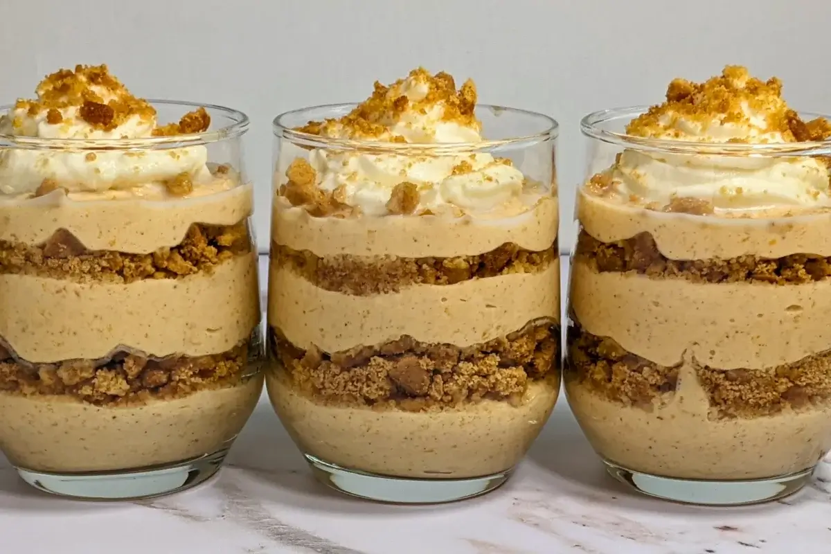 Pumpkin yogurt parfait cups layered with pumpkin yogurt, gingersnap biscuits, and topped with whipped cream.