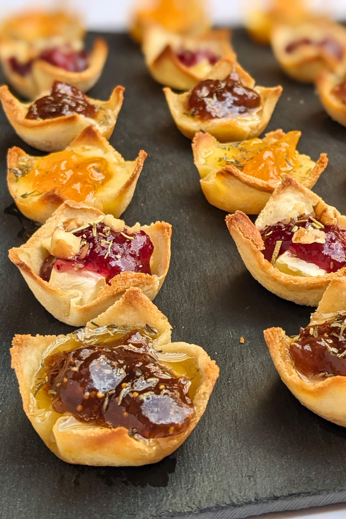 Trio of cheese and jam appetizers in mini toast cups - mini bread toast cups filled with Brie cheese and cranberry jam, Parmesan cheese and fig jam, and cheddar cheese and apricot jam, topped with crushed walnuts and a honey-dried thyme drizzle.