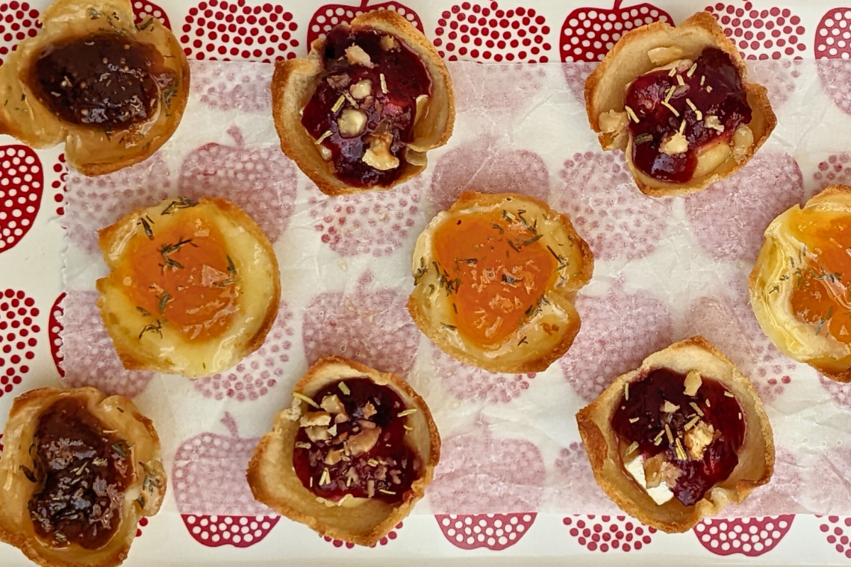 Trio of cheese and jam appetizers in mini toast cups - mini bread toast cups filled with Brie cheese and cranberry jam, Parmesan cheese and fig jam, and cheddar cheese and apricot jam, topped with crushed walnuts and a honey-dried thyme drizzle.