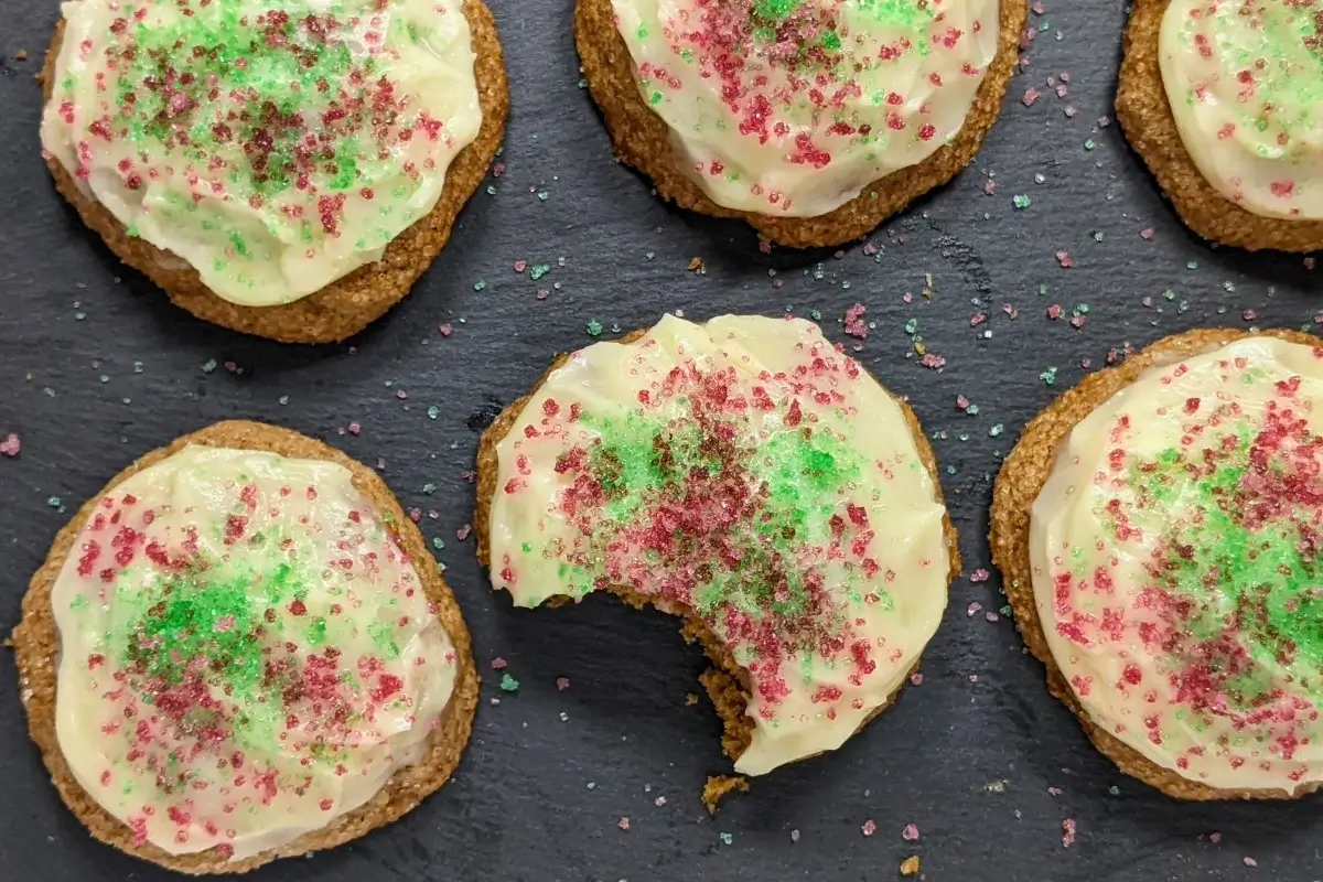 Christmas pumpkin sugar cookies made with healthier wholemeal flour and coconut sugar, frosted with a classic butter and cream cheese icing, and decorated with red and green sugar sprinkles.