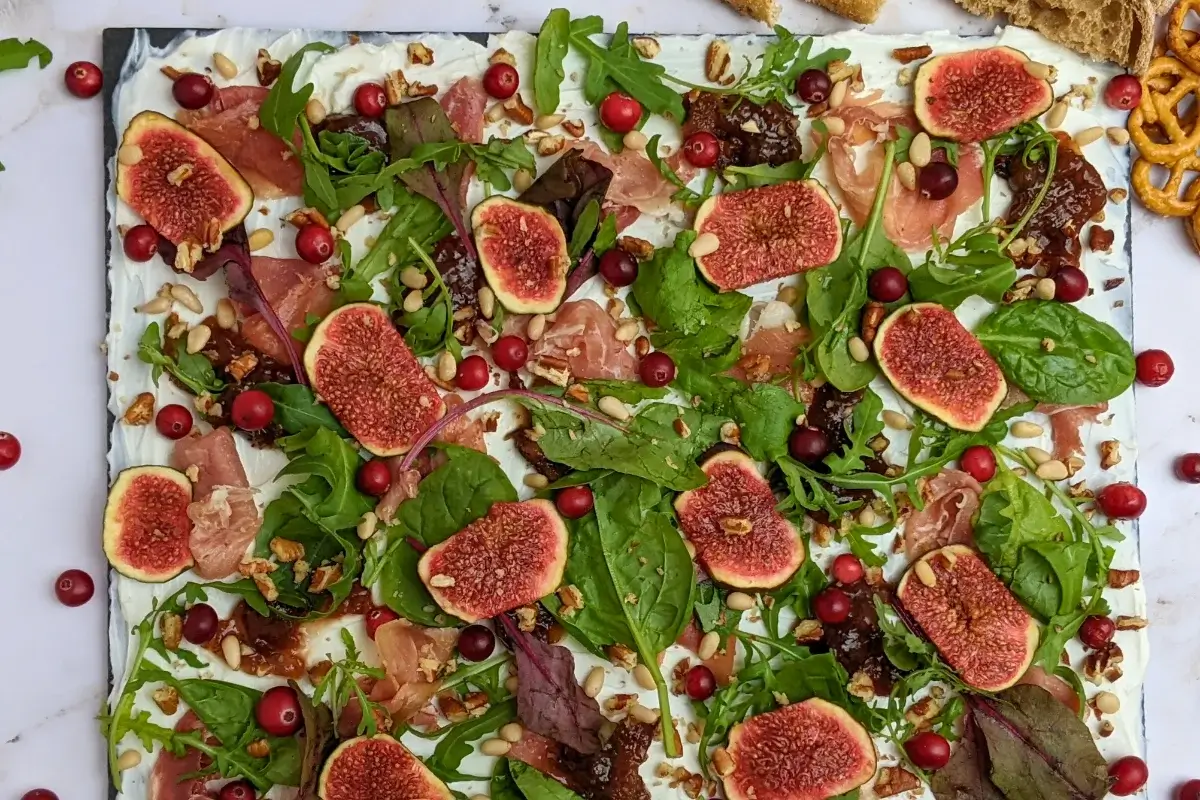 Fig and Goat Cheese Appetizer "Butter" Board With Prosciutto - appetizer board with fresh figs, fig jam, prosciutto, and crunchy toppings sprinkled over a whipped goat cheese spread on a party platter.