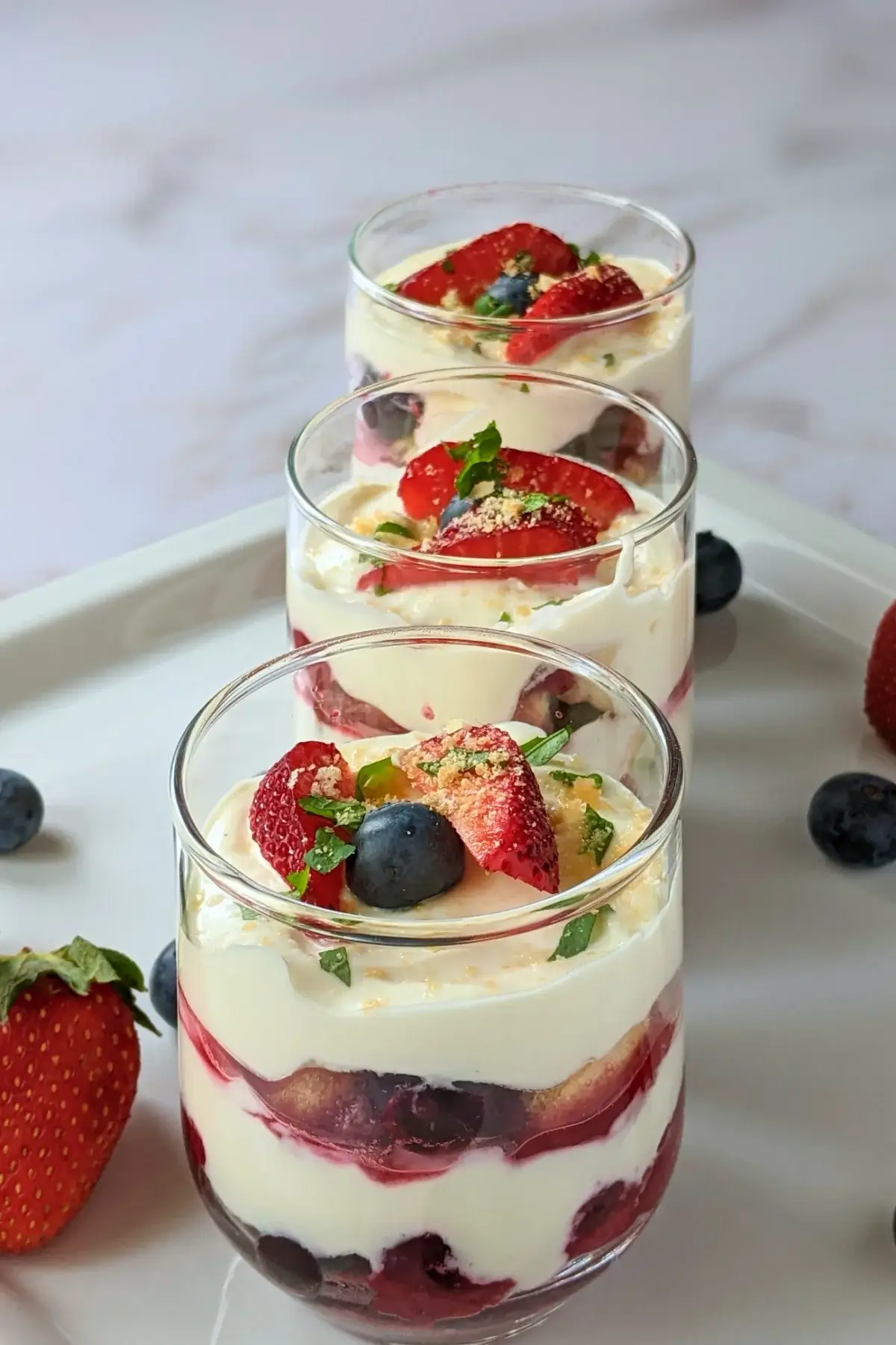 Mixed berry tiramisu in a glass dish with layers of mascarpone, Greek yogurt, and cooked berries like blueberries and strawberries.