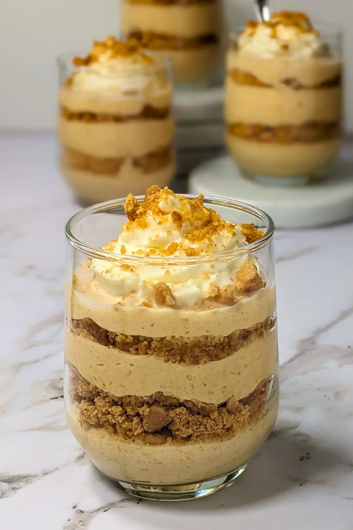 Pumpkin yogurt parfait cups made and layered with pumpkin Greek yogurt, gingersnap biscuits, and topped with whipped cream.