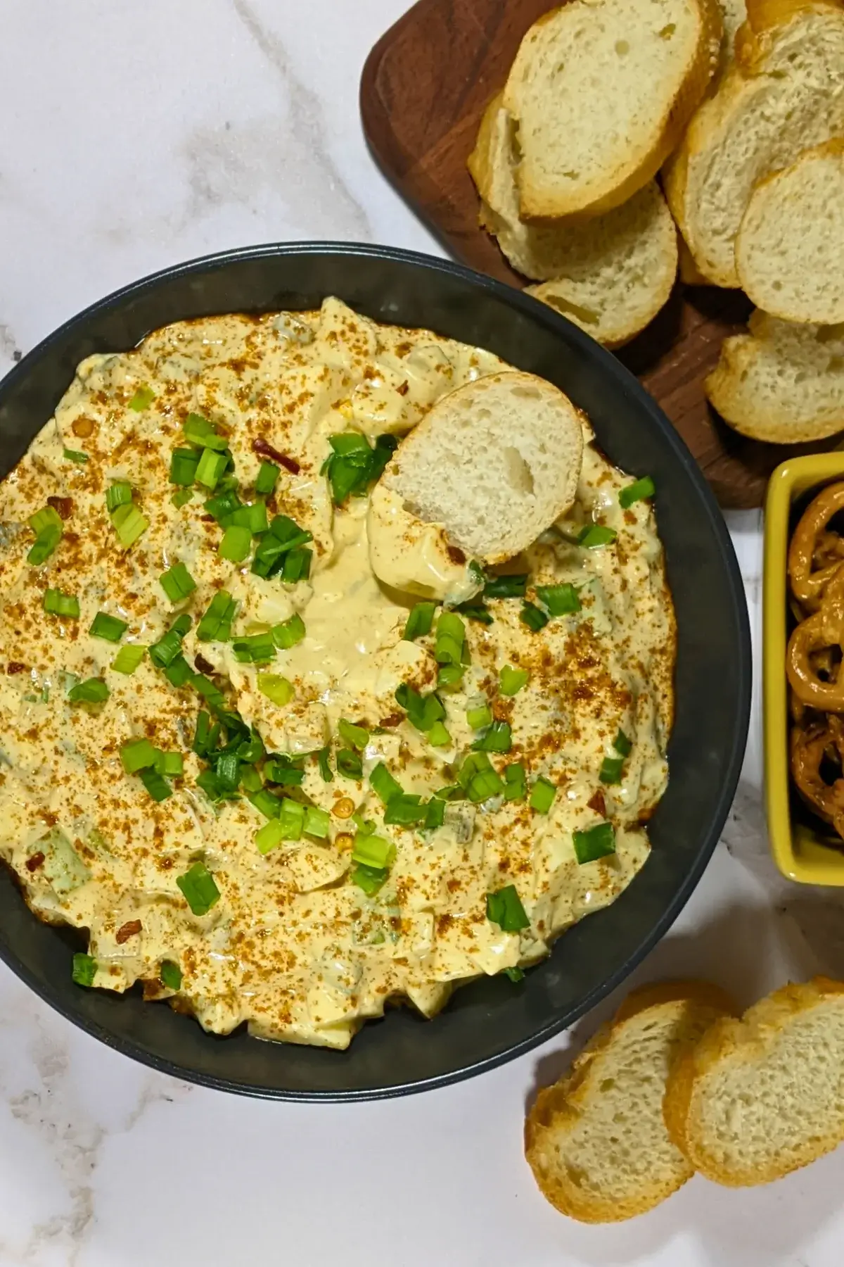Deviled Egg Dip - party dip made with a creamy blend of mashed hard-boiled eggs, mayonnaise, mustard, seasonings like salt, pepper, and paprika, and topped with chopped green onion, served with pretzels and toasted bread.