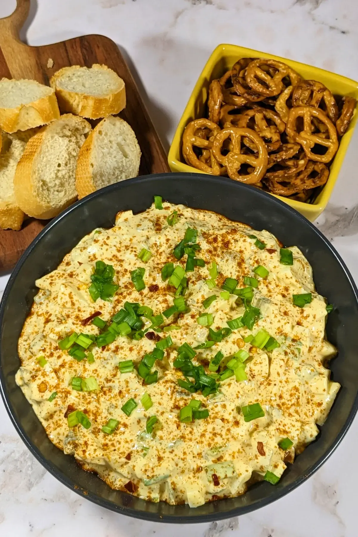 Deviled Egg Dip - party dip made with a creamy blend of mashed hard-boiled eggs, mayonnaise, mustard, seasonings like salt, pepper, and paprika, and topped with chopped green onion, served with pretzels and toasted bread.