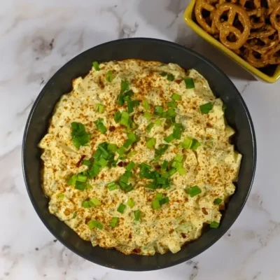 Deviled Egg Dip - party dip made with a creamy blend of mashed hard-boiled eggs, mayonnaise, mustard, seasonings like salt, pepper, and paprika, and topped with chopped green onion, served with pretzels and toasted bread.