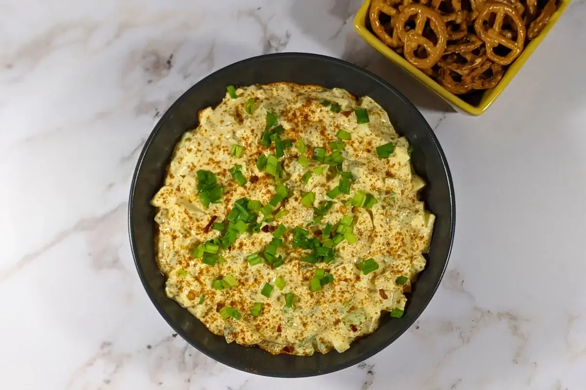Deviled Egg Dip - party dip made with a creamy blend of mashed hard-boiled eggs, mayonnaise, mustard, seasonings like salt, pepper, and paprika, and topped with chopped green onion, served with pretzels and toasted bread.