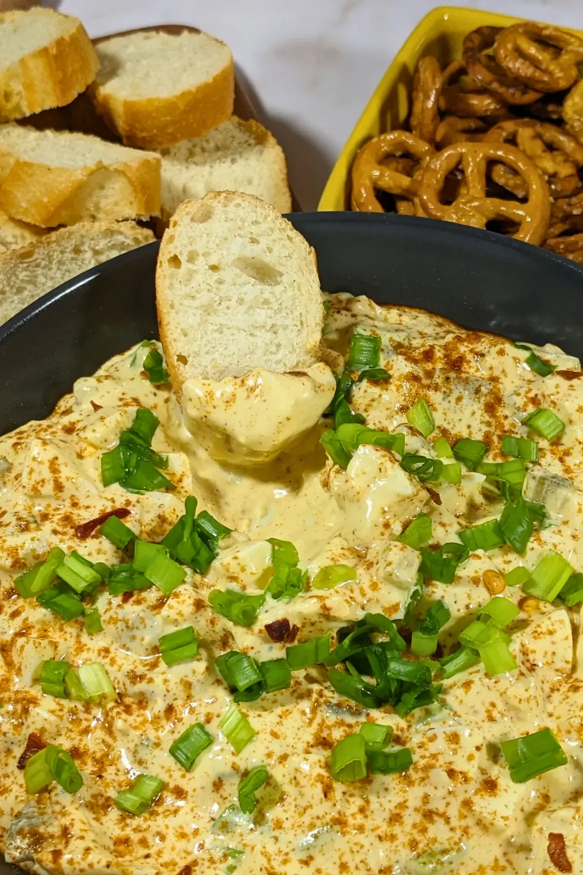 Deviled Egg Dip - party dip made with a creamy blend of mashed hard-boiled eggs, mayonnaise, mustard, seasonings like salt, pepper, and paprika, and topped with chopped green onion, served with pretzels and toasted bread.