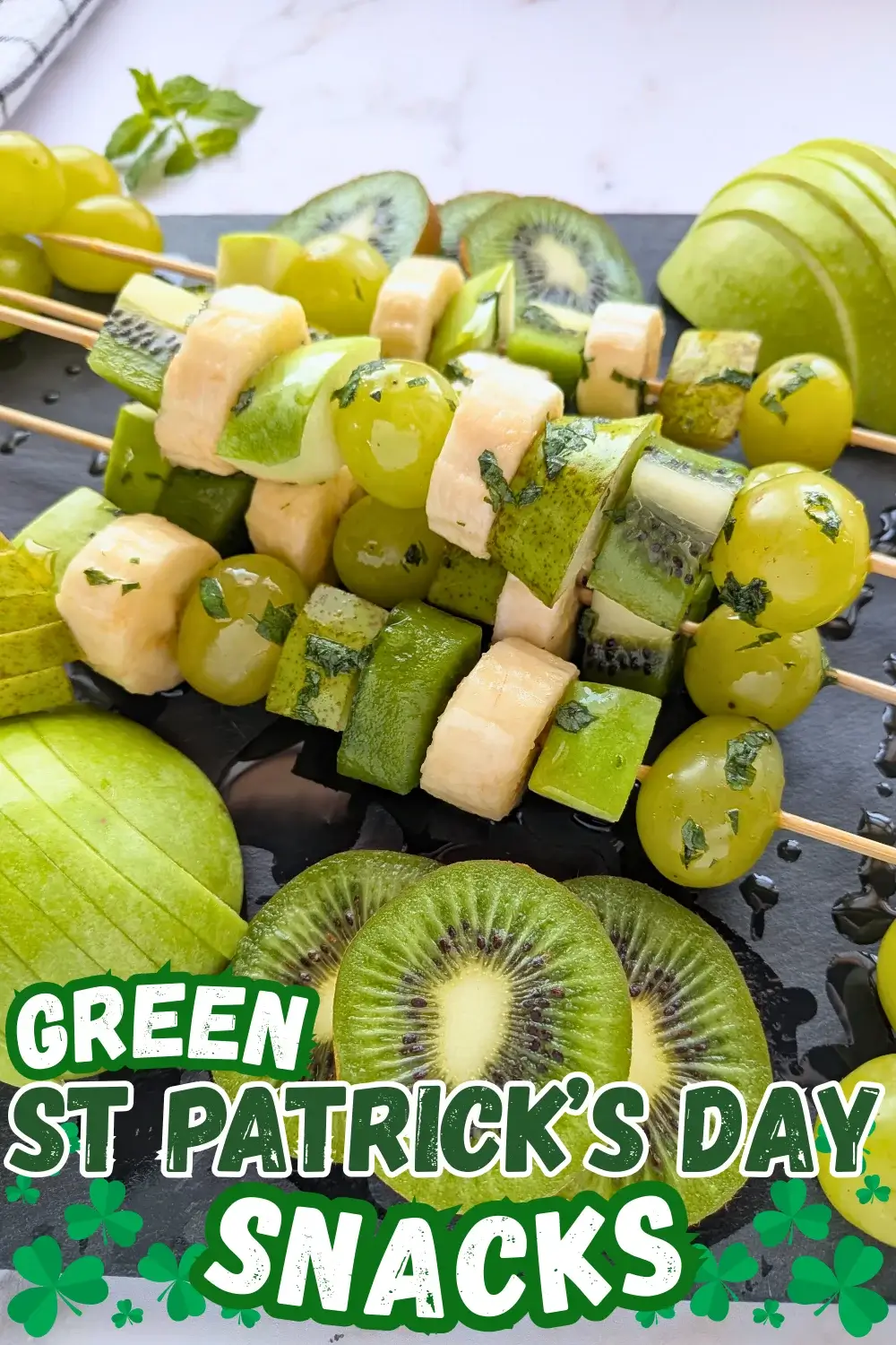 Green Fruit Tray - colorful green-themed fruit tray with green fruit kabobs featuring fruits like kiwi, green grapes, green apple, green pear, and bananas that are drizzled with a fresh mint, lime juice, and maple sryup sauce, plus slices of green apple, green pear, kiwis, and little piles of green grapes.