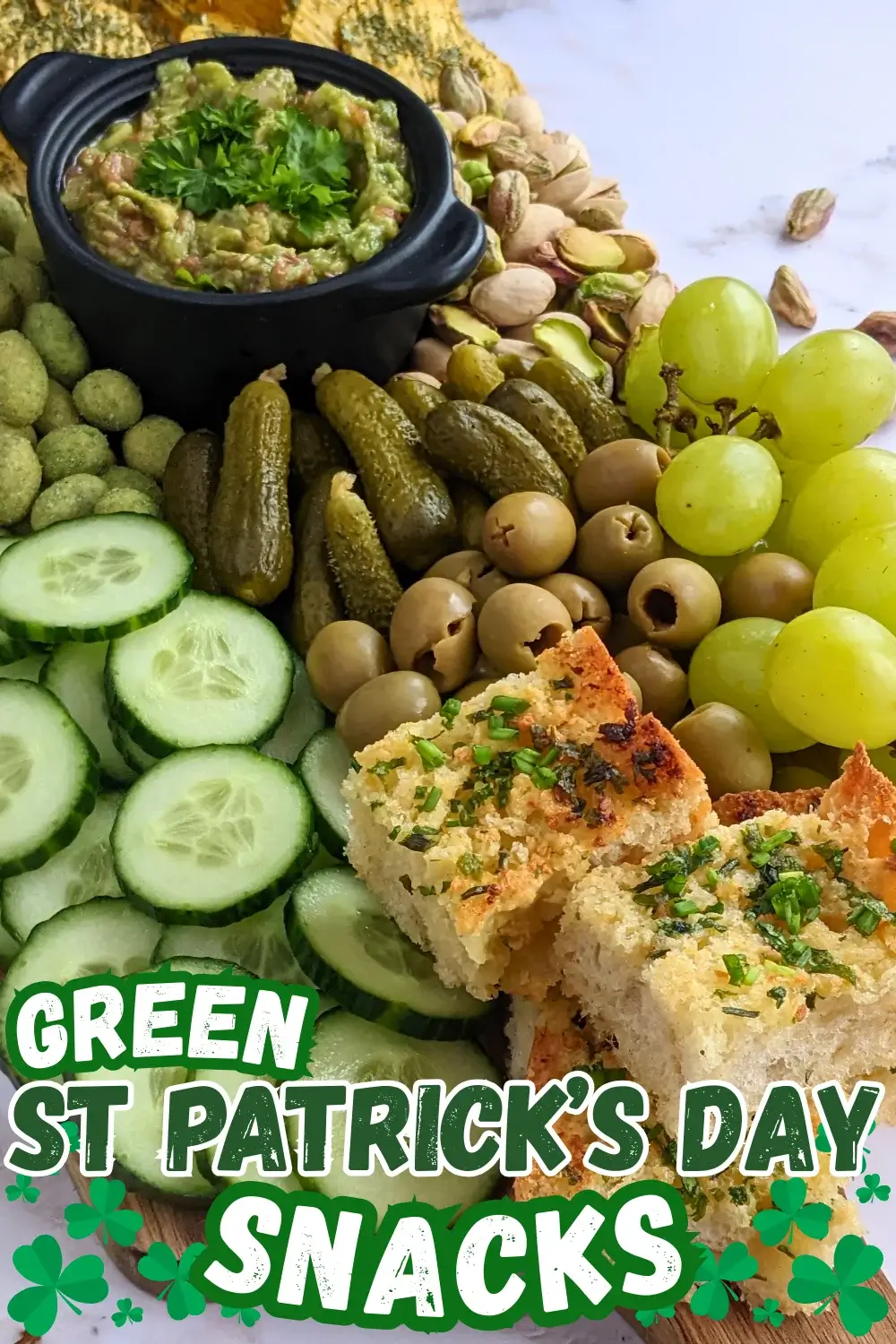 Green Snack Board - Green themed snack board and party tray with homemade garlic bread and guacamole dip, dried chives covered potato chips, fresh cucumbers, mini pickles, olives, pistachios, crunchy wasabi coated peanuts, and green grapes.