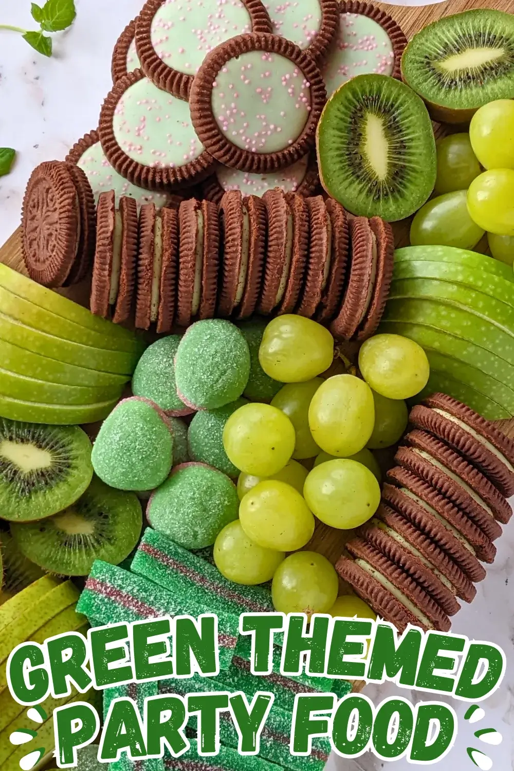 Green Themed Dessert Charcuterie Board - Green themed dessert tray with fresh fruit like green grapes, sliced green apples, kiwis, and green pears, a selection of green gummy candies, and lime flavored and peppermint filled Domino cookies.